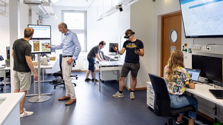 KI-Labor, Person mit VR-Brille und andere Personen an PCs