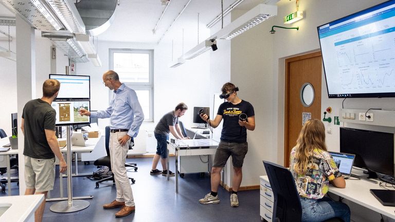 KI-Labor, Person mit VR-Brille und andere Personen an PCs
