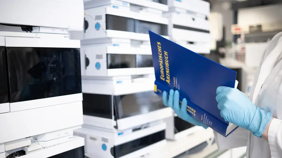 Titelbild: Labor, Person in Laborkittel mit Buch vor Laborgeräten