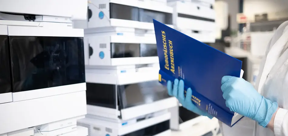 Titelbild: Labor, Person in Laborkittel mit Buch vor Laborgeräten