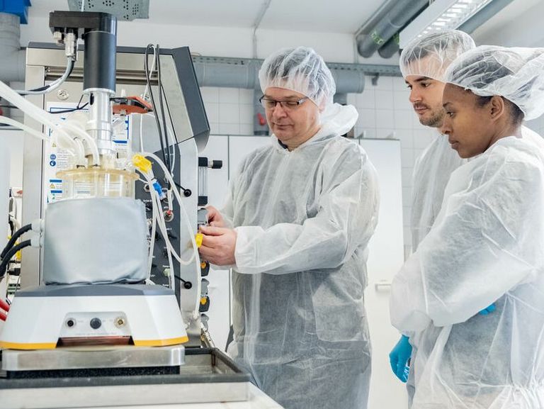 Personen im Laborkittel, Handschuhen und Haarhaube im Labor