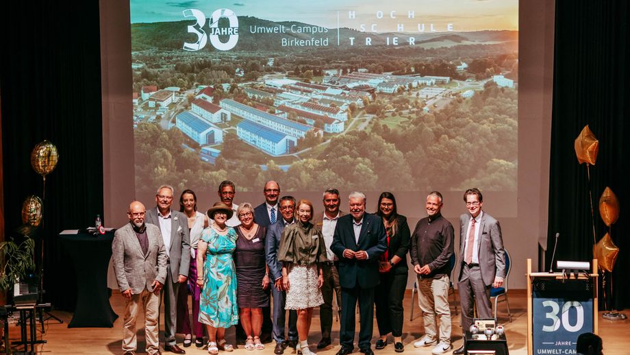 Das Präsidium der Hochschule Trier mit Campusleitung und Ehrengästen auf der Bühne der Aula, u. a. mit Kurt Beck (4. v. r.) und Staatssekretärin Dr. Tamara Müller (3. v. l) und Dr. Otto Schulz (rechts).